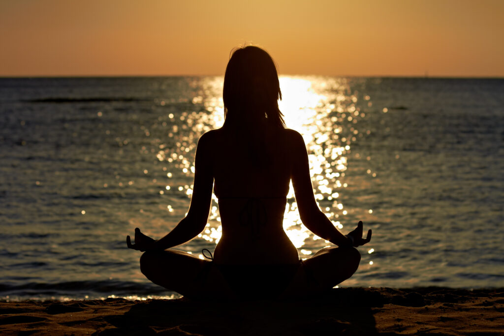Silhouette of woman in yoga lotus meditation position front to seaside